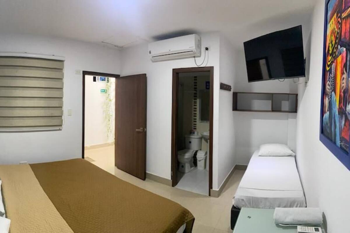 Ein Hotelzimmer mit Bett, Schreibtisch mit Stuhl, Wandfernseher und einem durchgegangenen Tür sichtbaren Badezimmer.