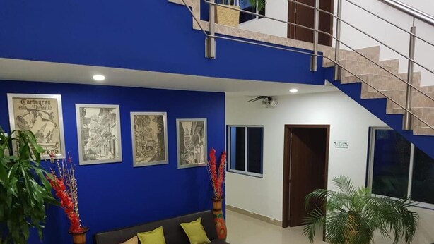 Un vestíbulo moderno con una pared azul de acento, un sofá negro con cojines amarillos y una escalera.