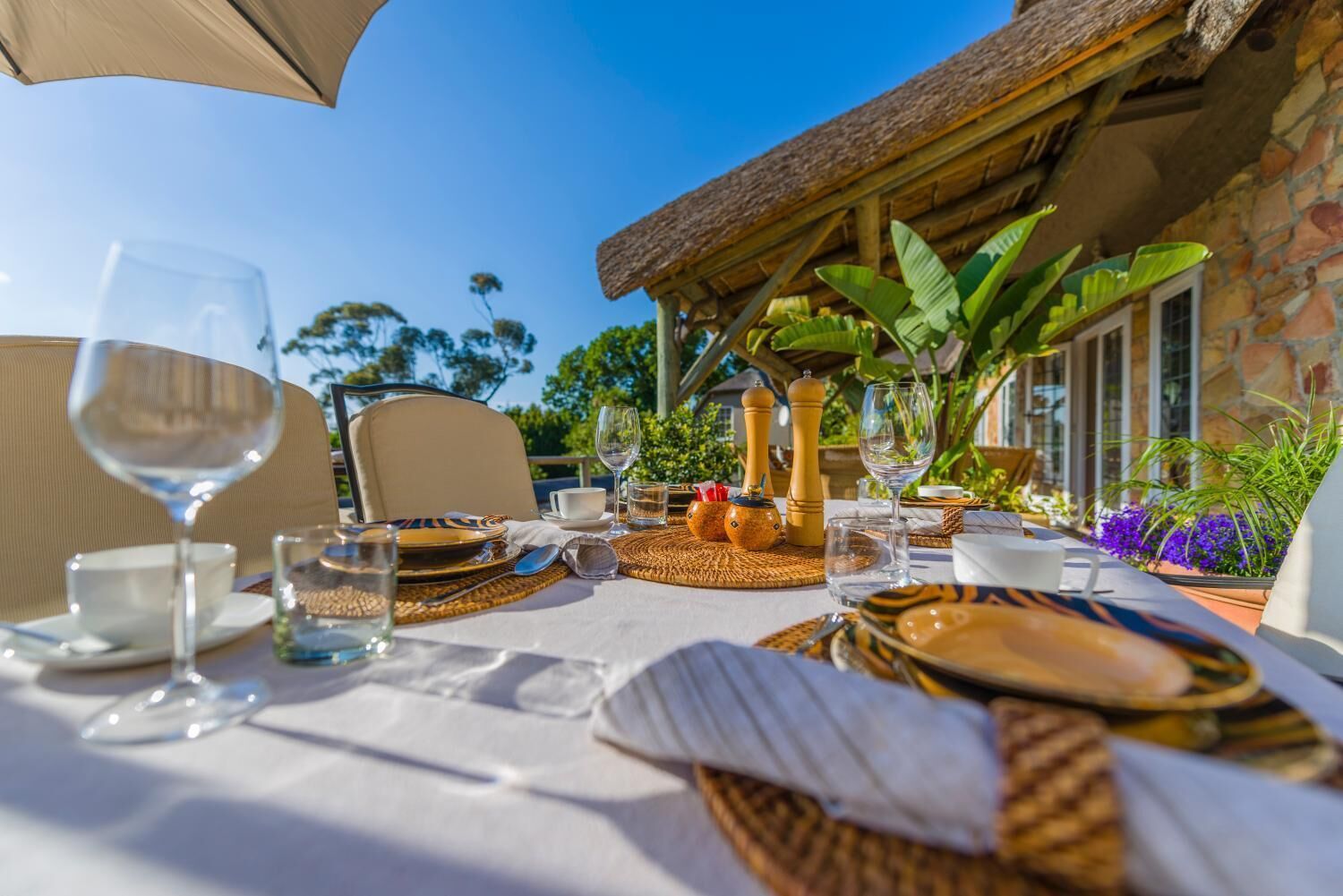 An outdoor dining area with a table set for two, featuring woven placemats, plates, and glasses.