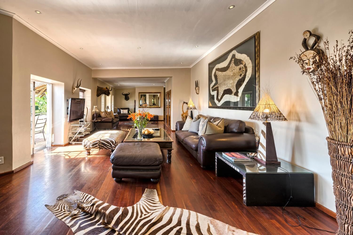 A spacious living room with a leather sofa, a zebra rug, and a large painting on the wall.