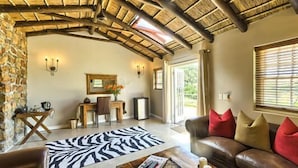 A spacious living room with a stone wall, a leather sofa, a zebra-patterned rug, and a dining area with a wooden table and chairs. - Ikhaya Safari Lodge (Cape Town)
