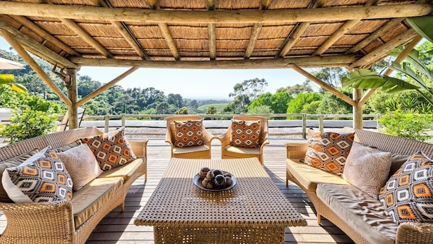 A covered outdoor seating area with wicker furniture and patterned cushions, overlooking a lush landscape. - Ikhaya Safari Lodge (Cape Town)