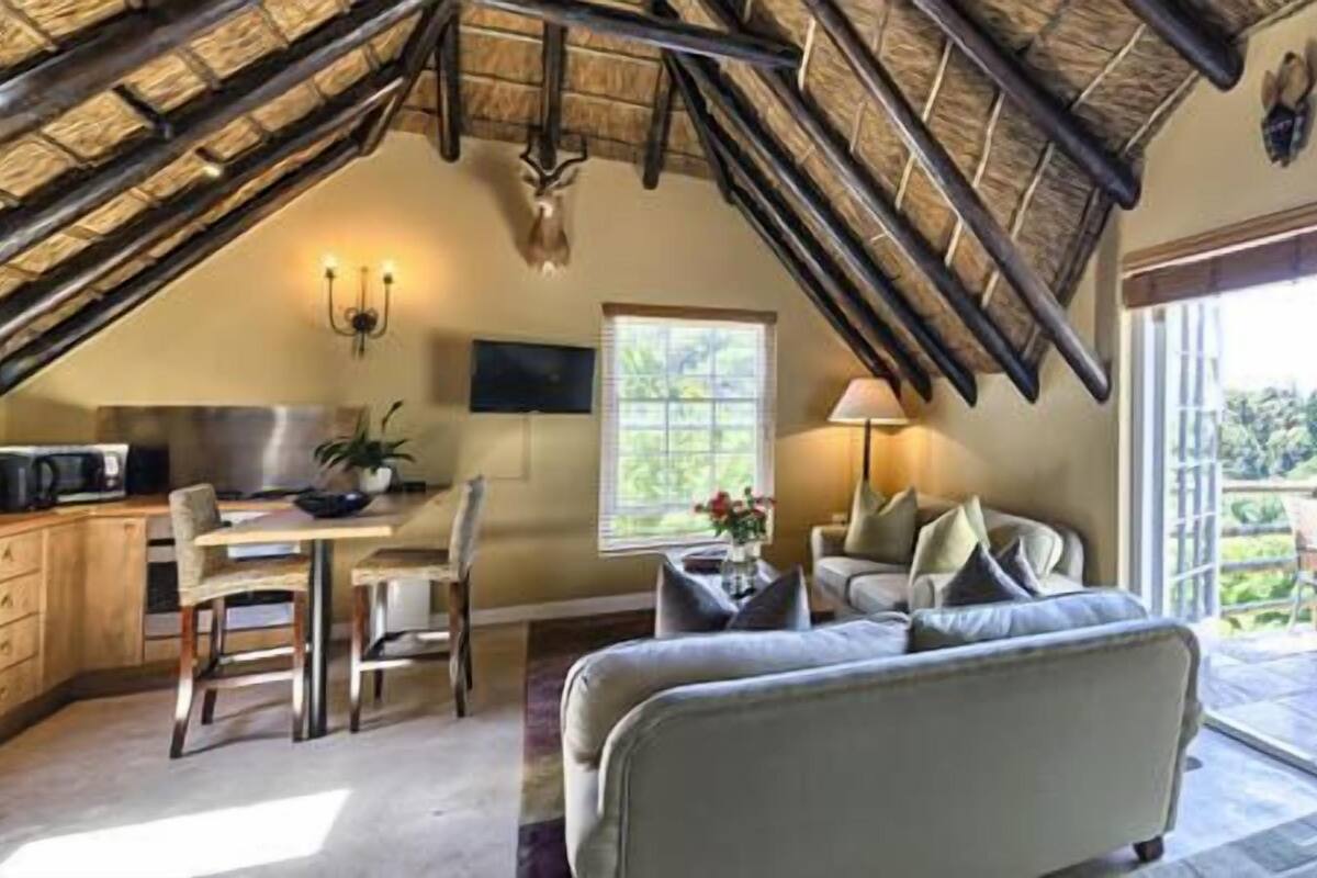 A cozy room with a sloped ceiling, a dining area, a sofa, and a view of greenery outside.
