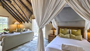 A bedroom with a canopy bed, a sofa, and a nightstand with lamps. - Ikhaya Safari Lodge (Cape Town)
