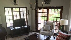 A living room with a TV, a chandelier, a clock, and a large window with blinds. - Benka Lifestyle (Lobamba)