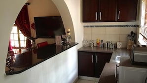 A compact kitchen with dark wooden cabinets, a black countertop, and a tiled backsplash. - Benka Lifestyle (Lobamba)