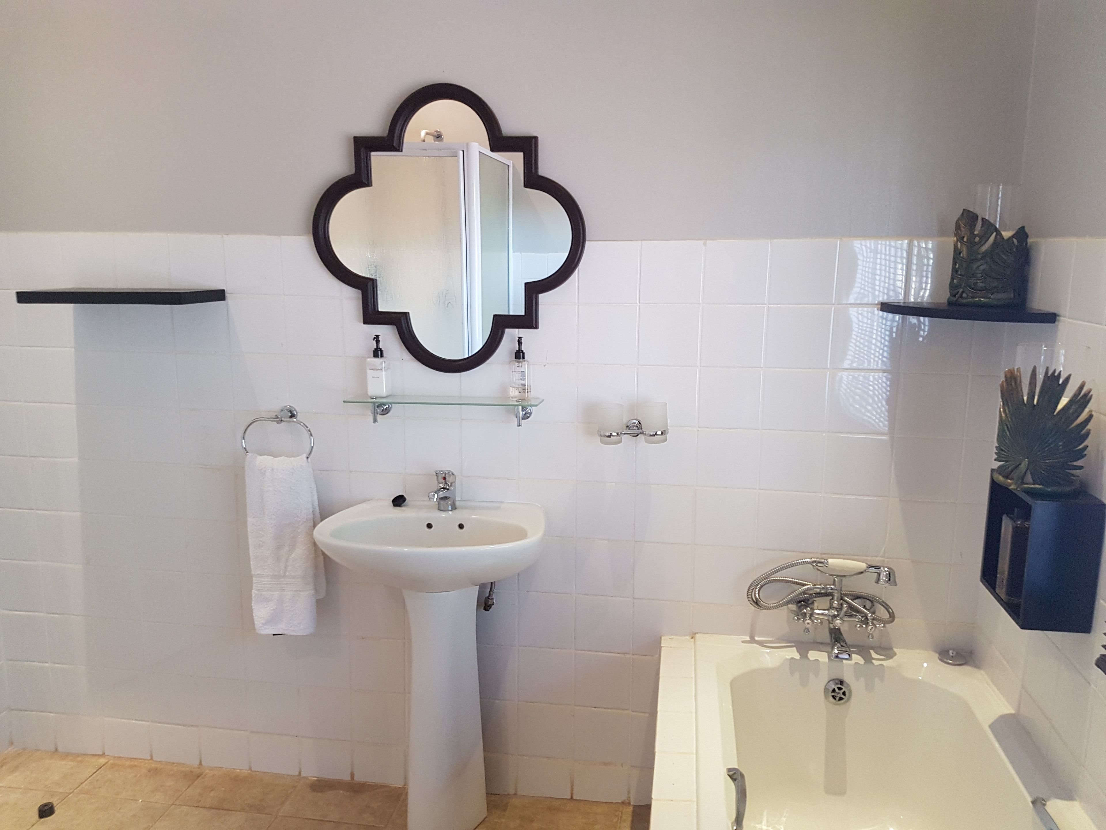 A bathroom with a white sink, a mirror, a bathtub, and a shelf with toiletries.