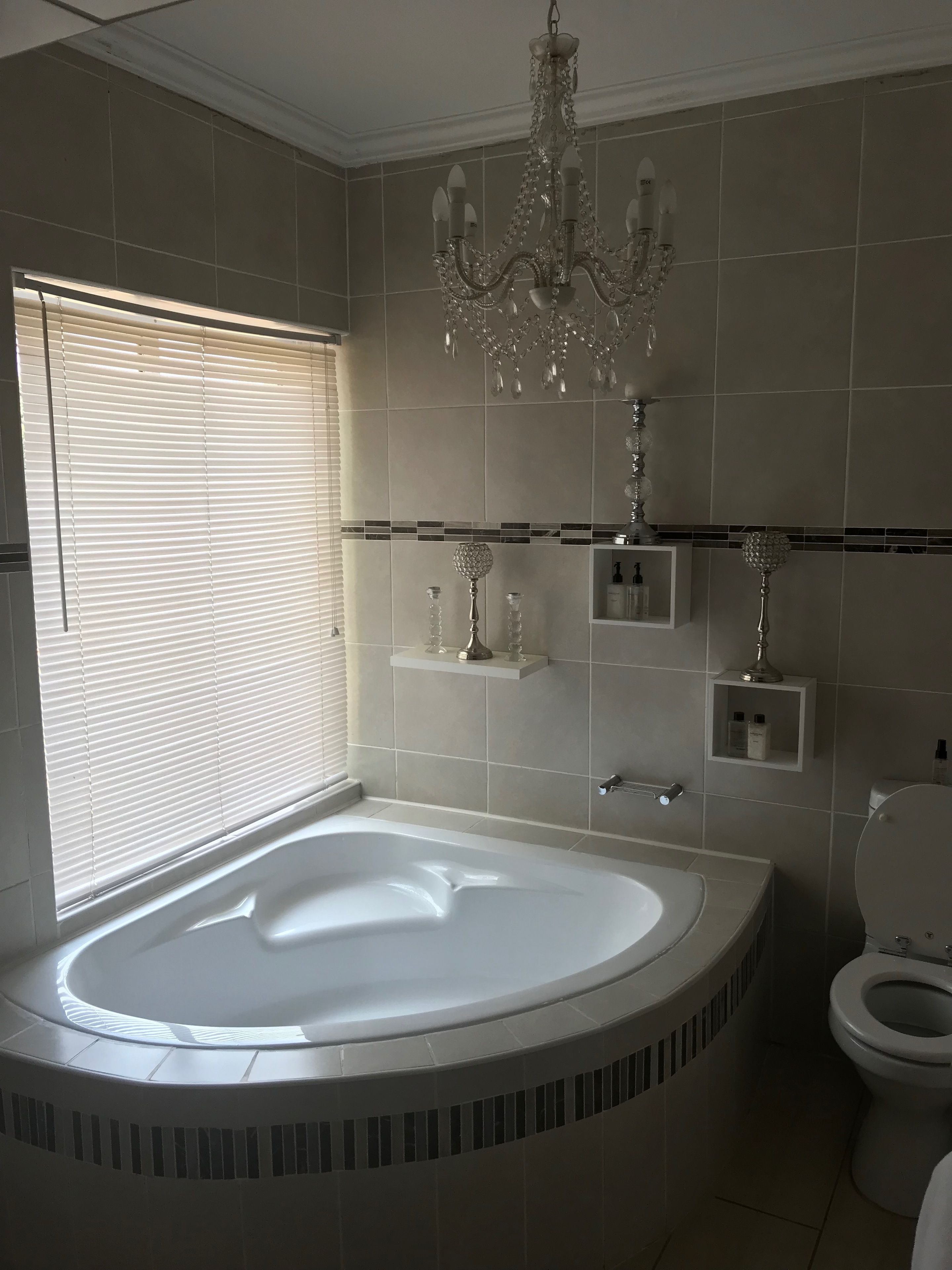 A bathroom with a freestanding bathtub, a toilet, a chandelier, and a window with blinds.