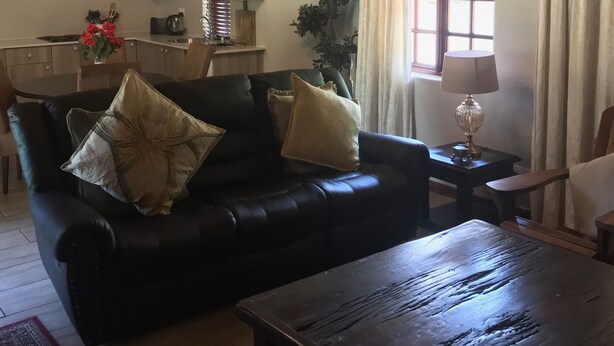 A living room with a black leather sofa, a wooden coffee table, and a chandelier. - Benka Lifestyle (Lobamba)