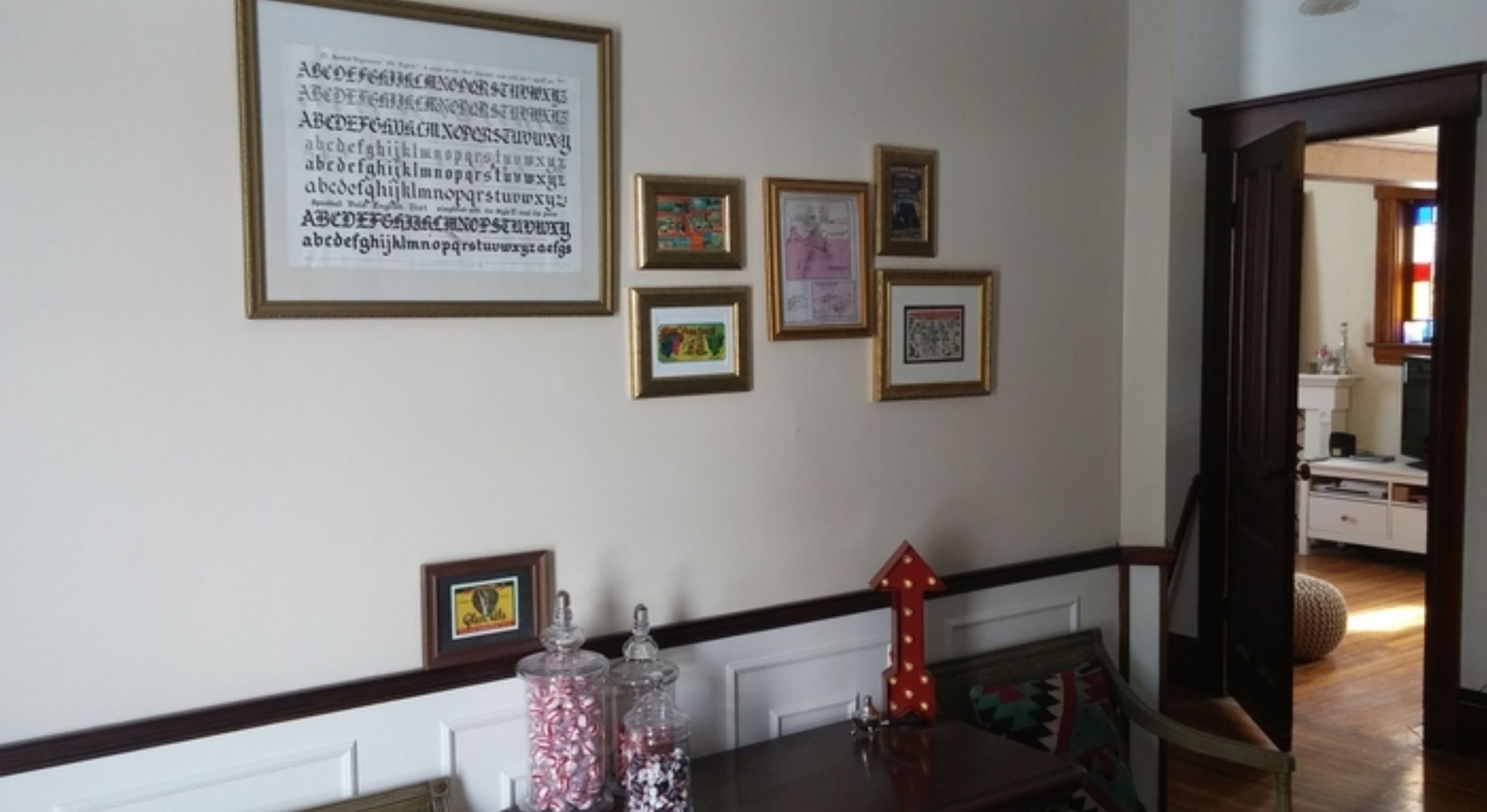 A dining area with a table set for two, a wall with framed pictures, and a door leading to another room.