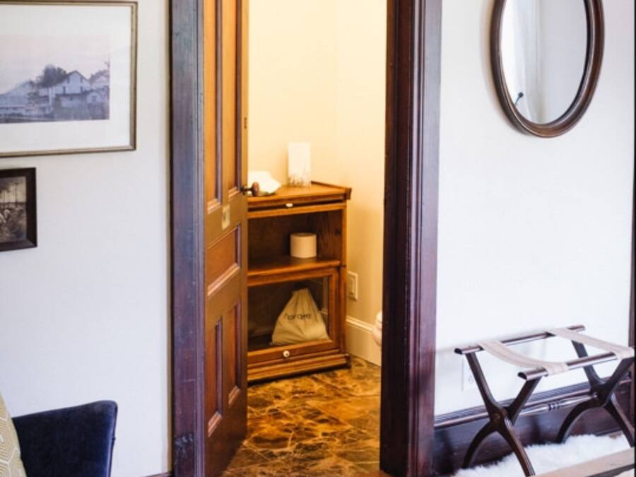Una puerta que da a un baño con puerta de madera, un perchero y un espejo en la pared.