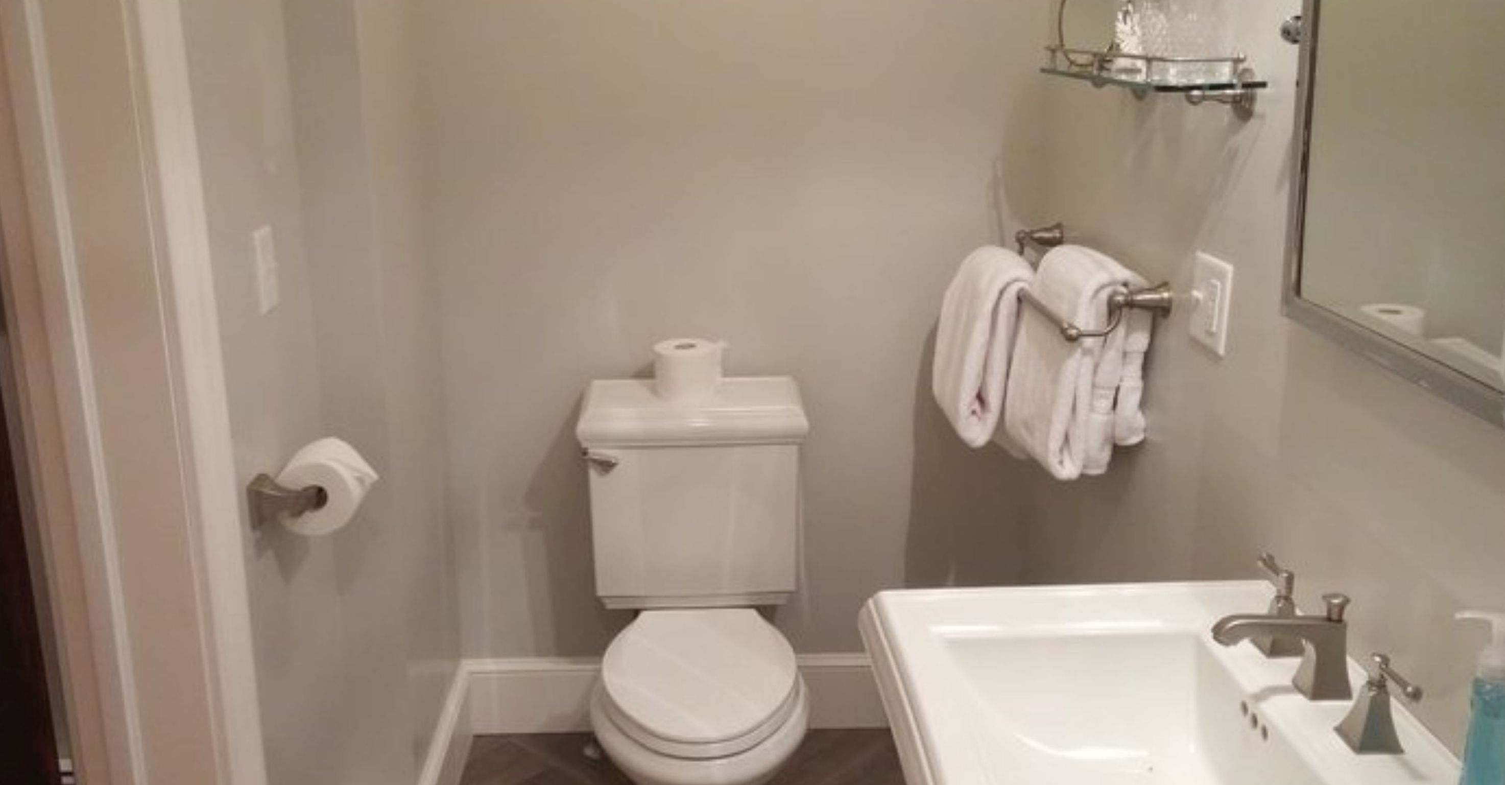 A bathroom with a toilet, a sink, and a glass shelf with toiletries.