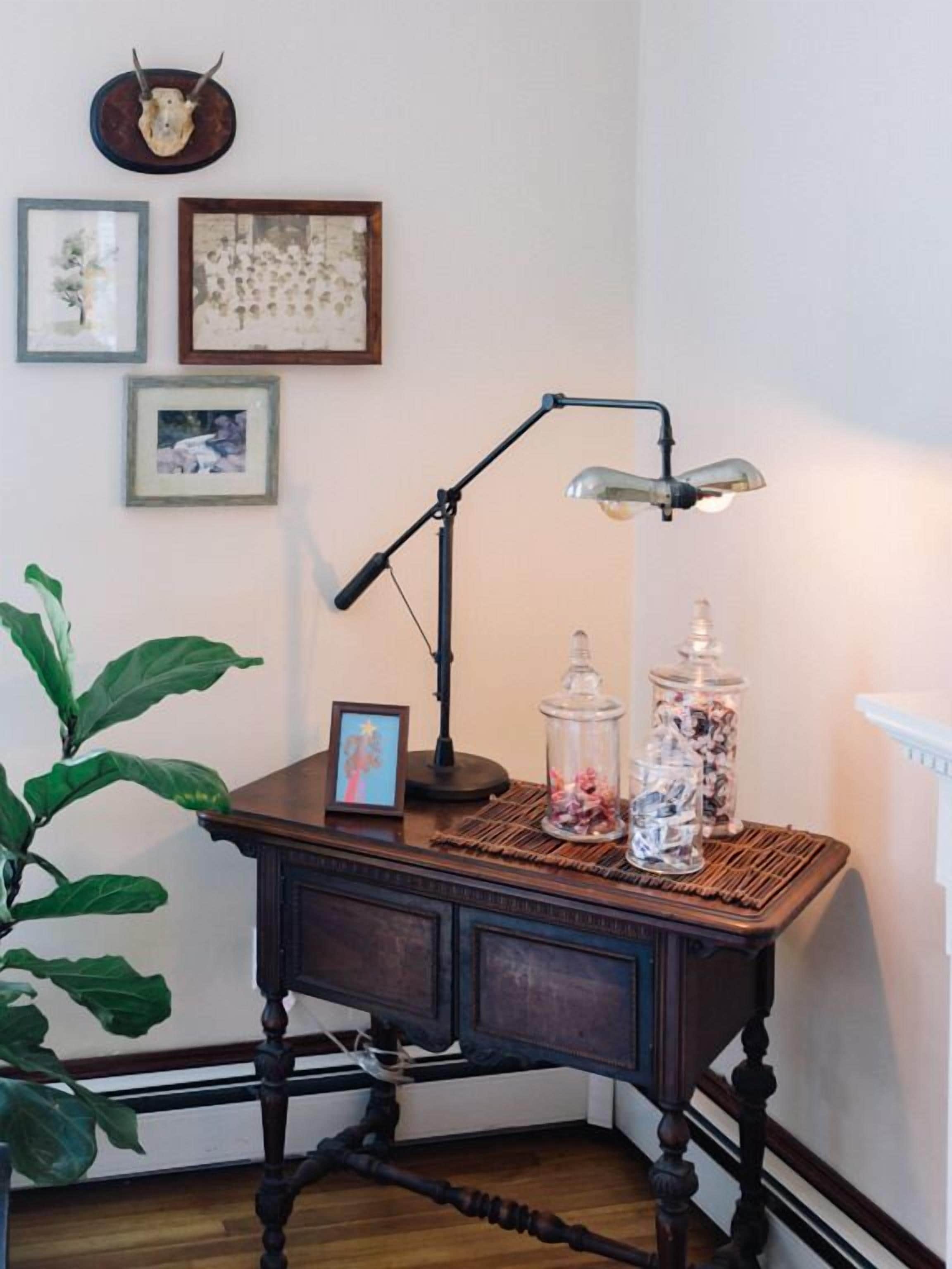 A wooden desk with a desk lamp, a picture frame, and two glass jars with decorative items.