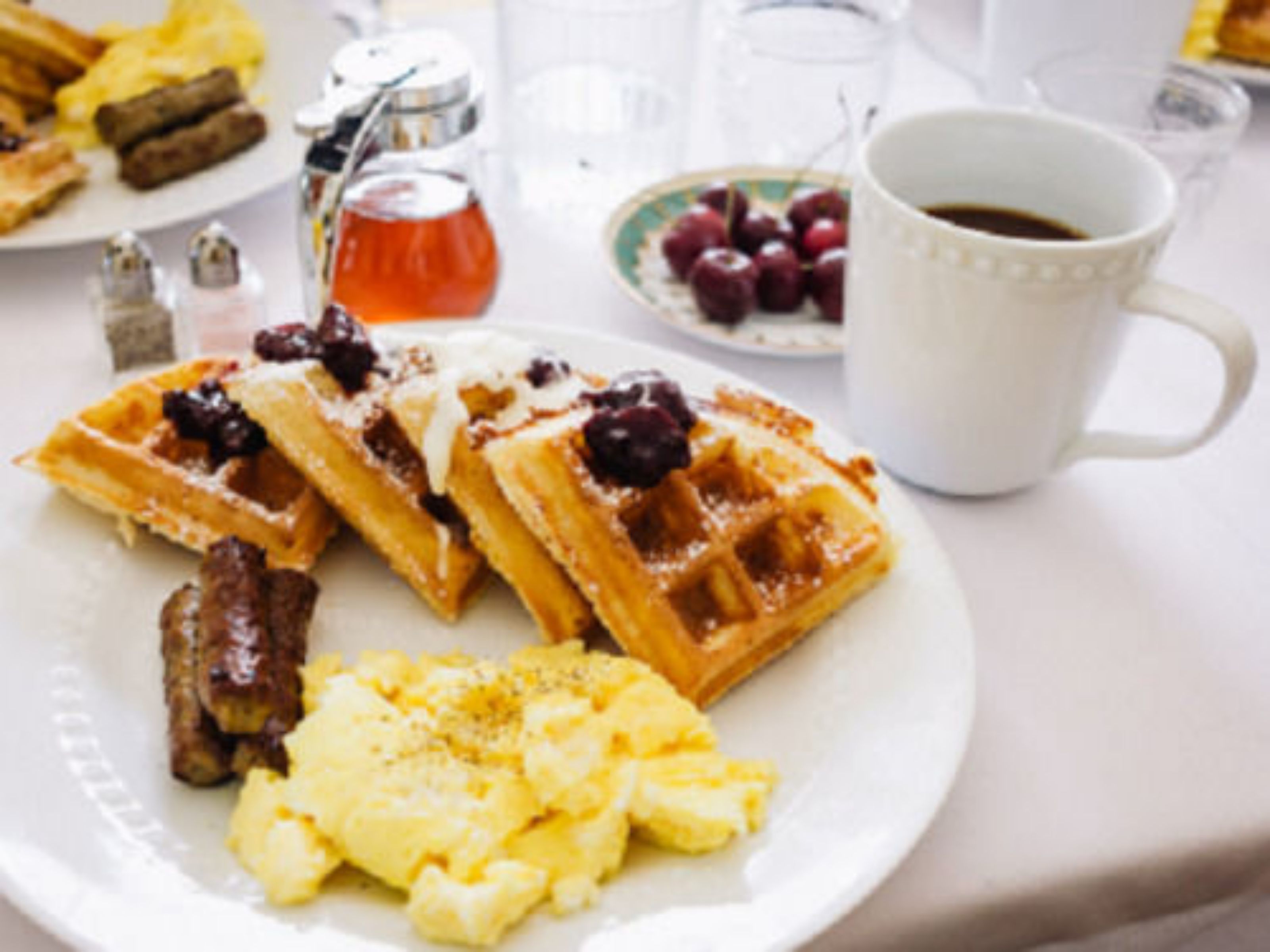 A breakfast plate with waffles, cherries, and scrambled eggs.