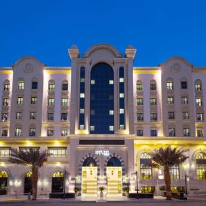 A large, multi-story hotel with a grand entrance, featuring a central archway and symmetrical facade.