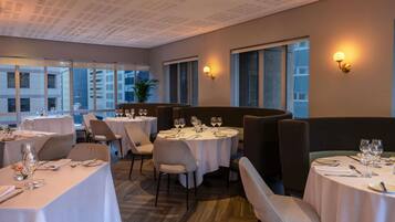 Un restaurante con mesas redondas, sillas y vistas a edificios a través de amplios ventanales.