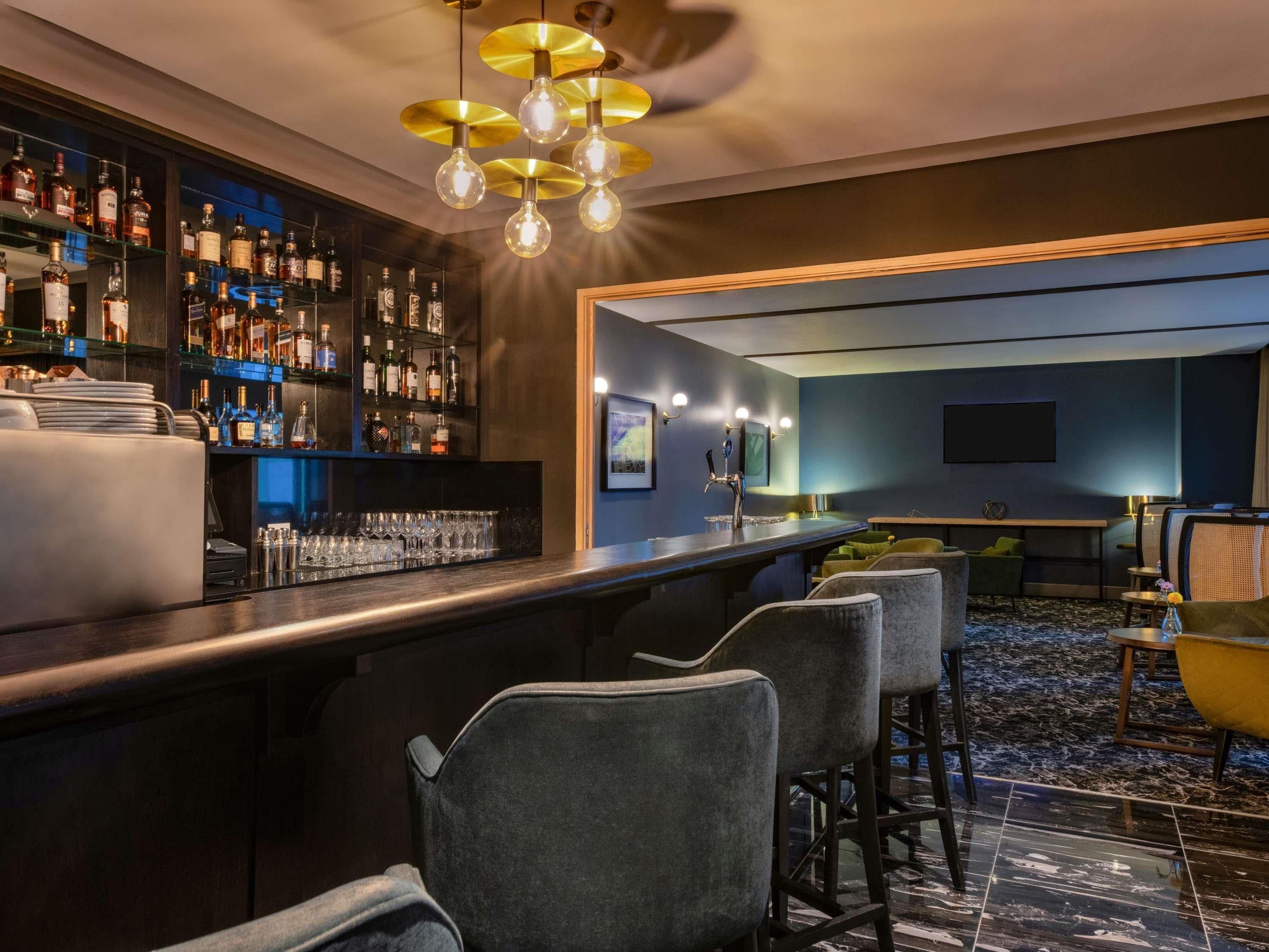 Uma área de bar com balcão, banquetas e prateleiras cheias de garrafas de bebidas.