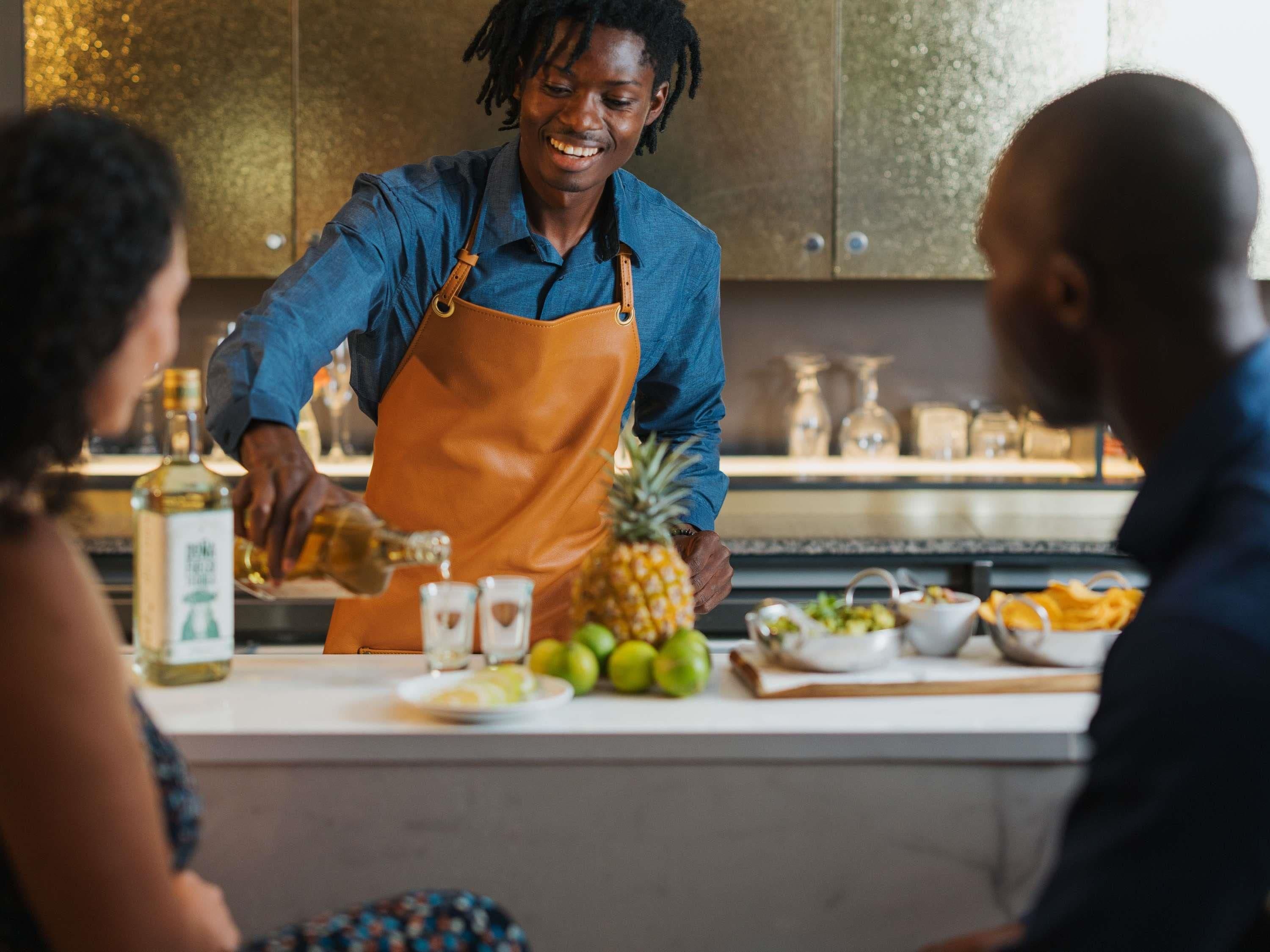 A person in an apron preparing drinks at a counter with various fruits and condiments.