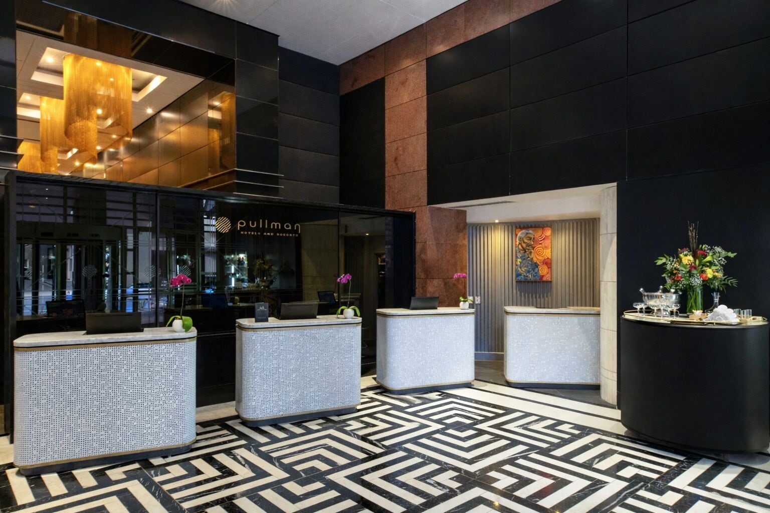 Zona de recepción de hotel con diseño moderno, que incluye un mostrador, una pantalla digital y un suelo con diseño.