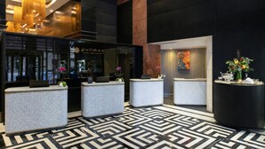 Zona de recepción de hotel con diseño moderno, que incluye un mostrador, una pantalla digital y un suelo con diseño.