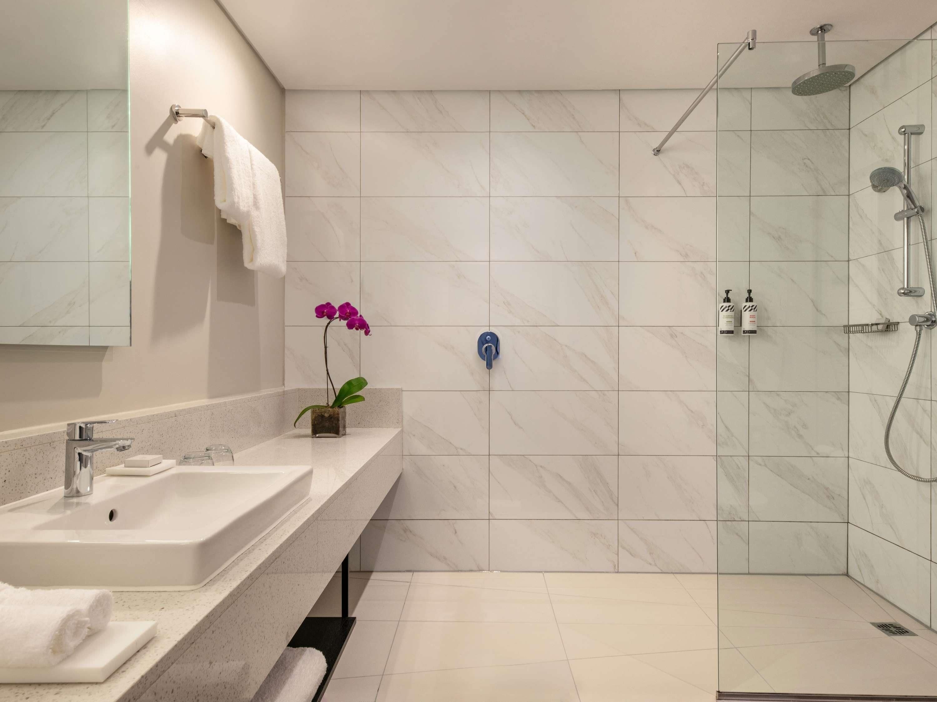 A modern bathroom with a shower, sink, and a potted orchid.