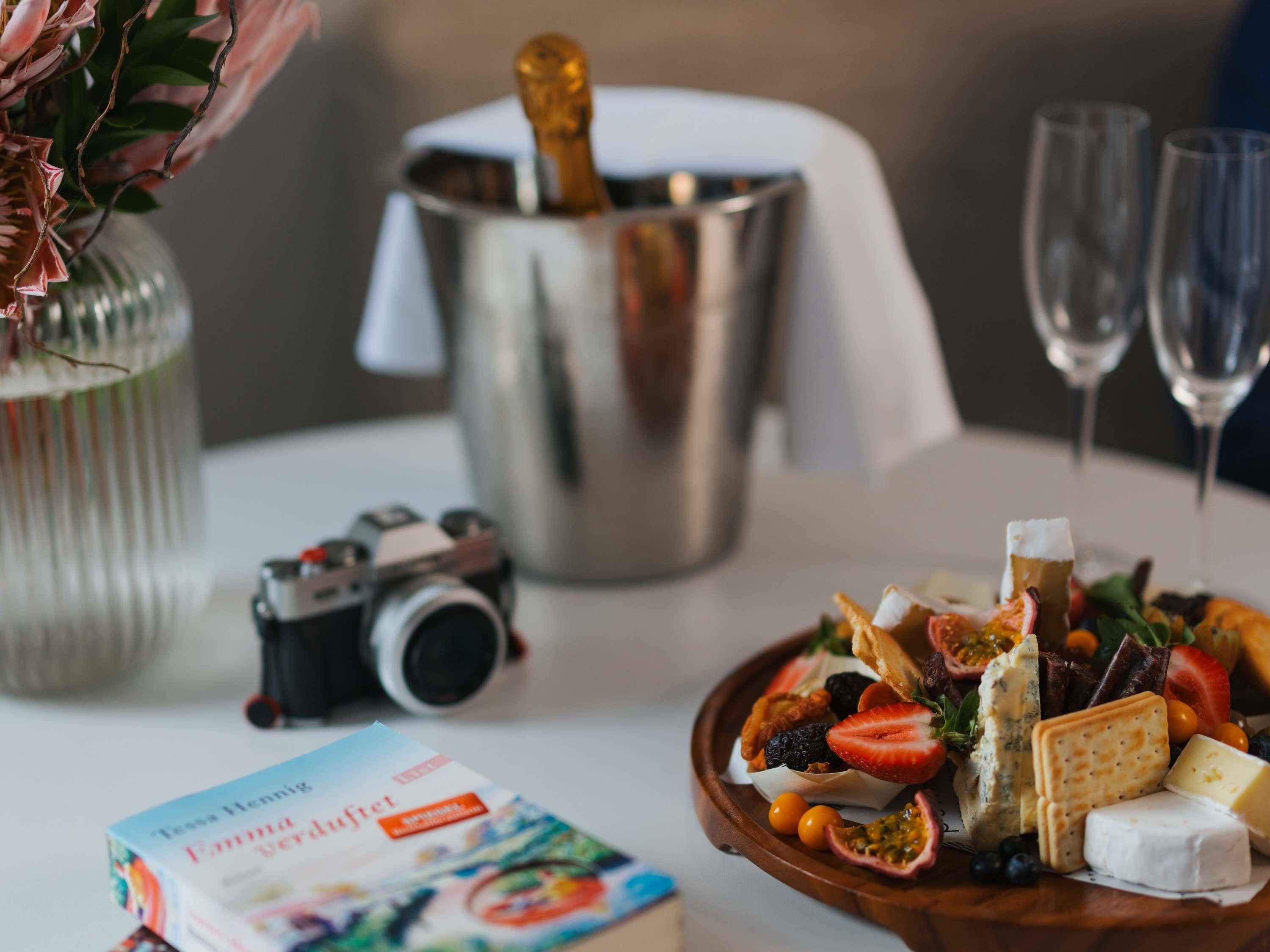 A table with a book, a camera, a champagne bottle, and a cheese platter.