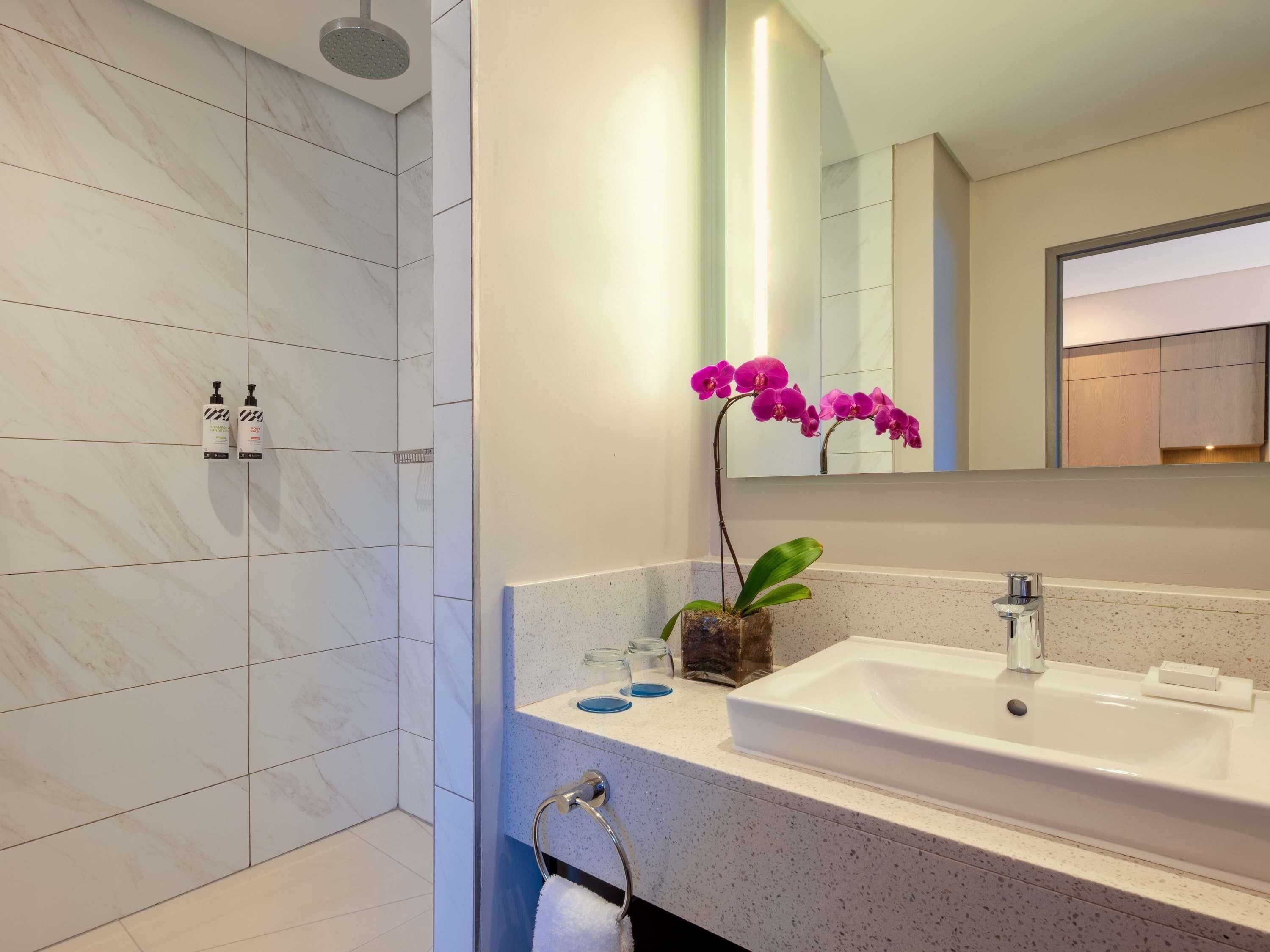 Une salle de bain moderne avec une douche en marbre blanc, un lavabo avec un miroir et une petite plante orchidée.