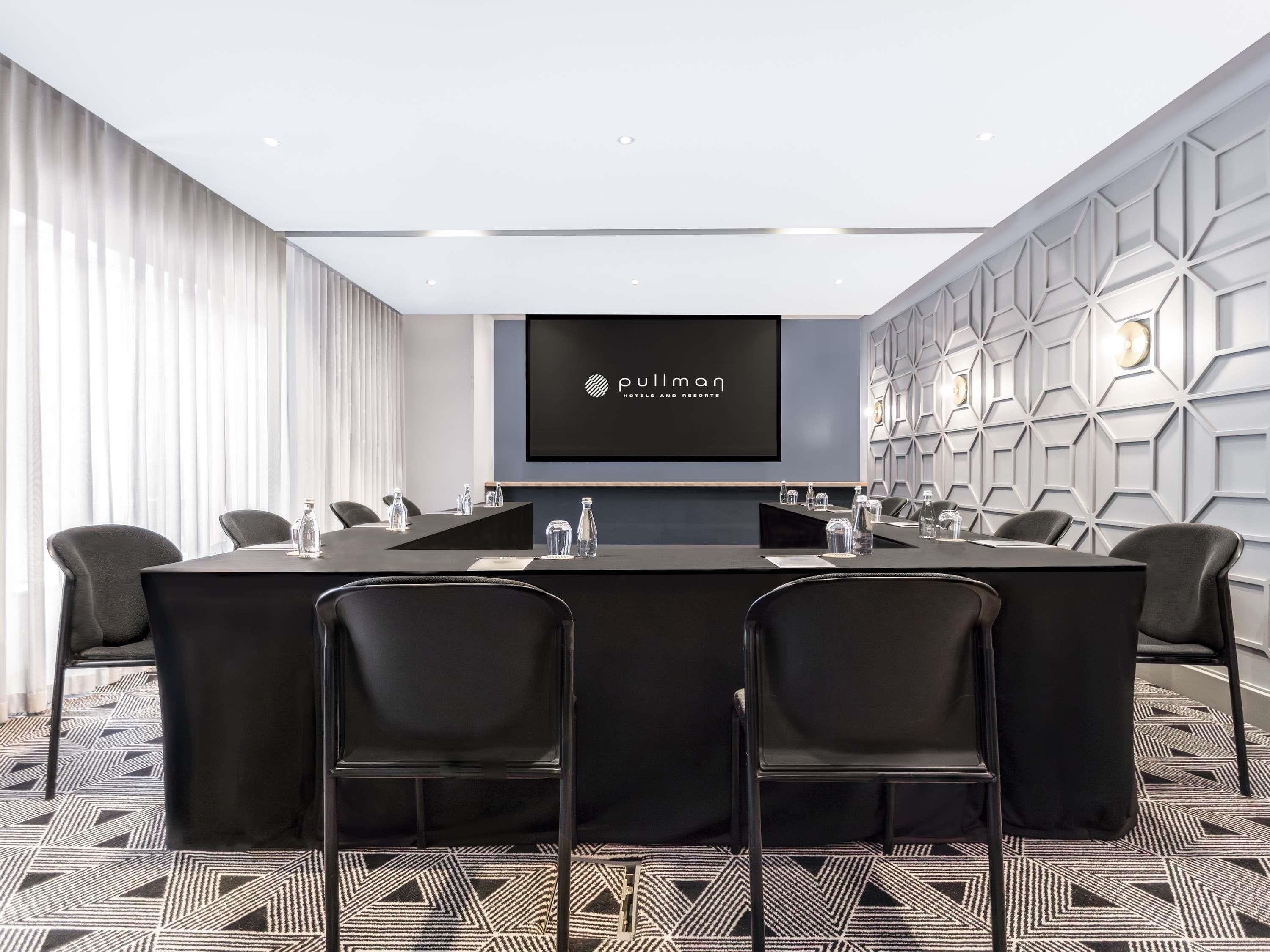 A conference room with a long table, chairs, a screen displaying 'Pullman Hotels and Resorts,' and a geometric wall design.