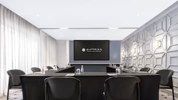 A conference room with a long table, chairs, a screen displaying 'Pullman Hotels and Resorts,' and a geometric wall design.
