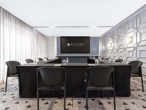 Un salón de conferencias con una larga mesa, sillas, una pantalla mostrando 'Pullman Hotels and Resorts' y un diseño geométrico en la pared.