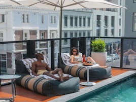 A rooftop pool area with two bean bag chairs, a table with drinks, and a potted plant.