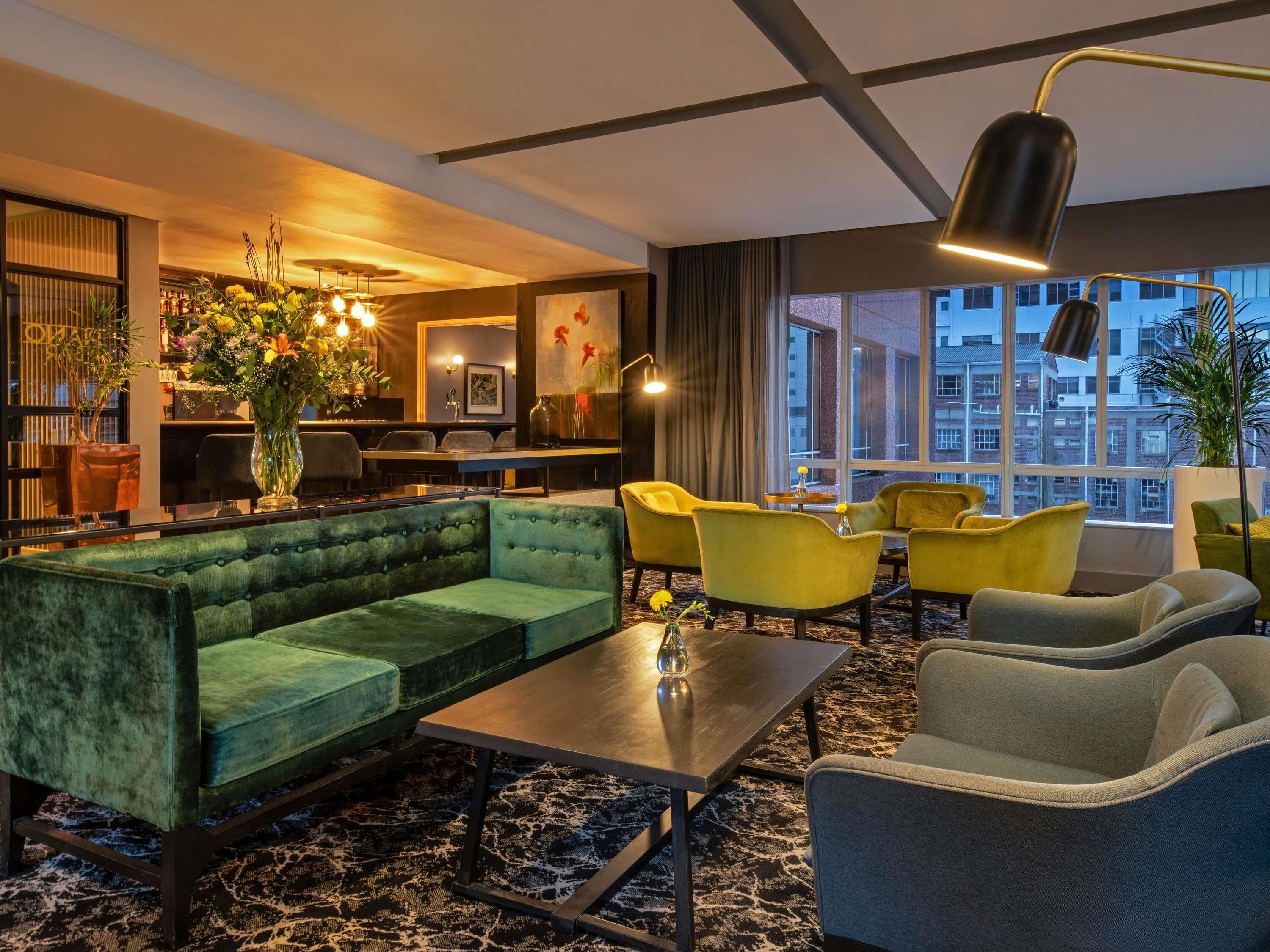 A modern lounge area with a green sofa, yellow chairs, and a marble-patterned floor.