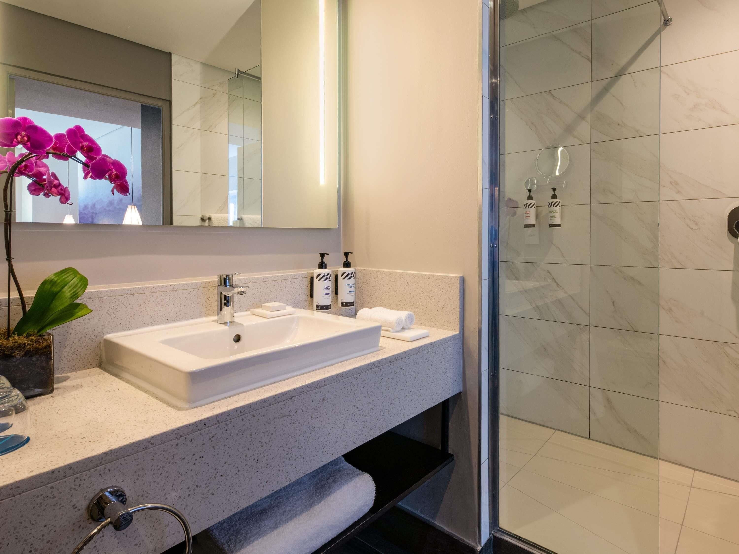 A modern bathroom with a white sink, a glass shower enclosure, and a potted orchid.