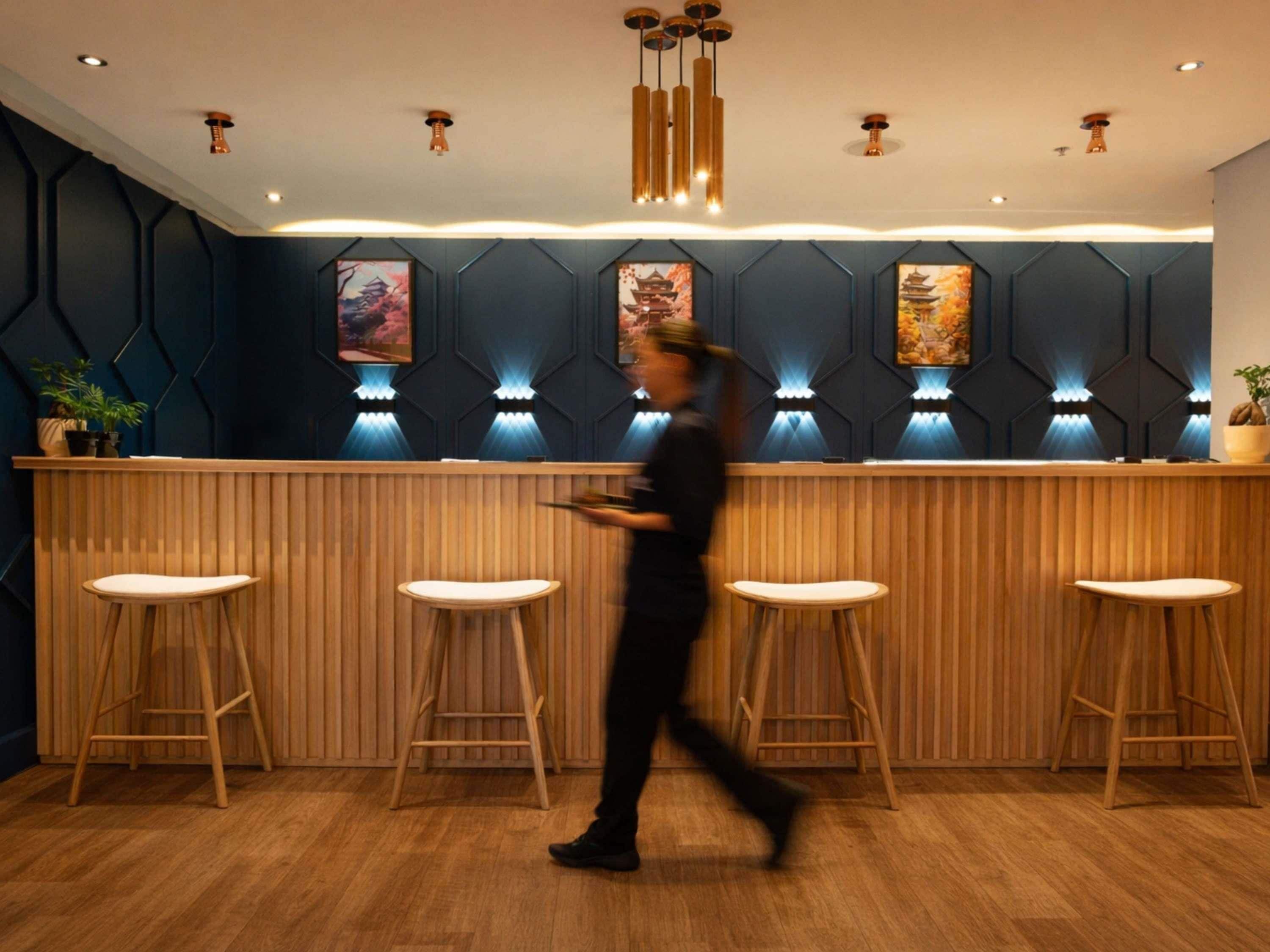 Un espace bar moderne avec un comptoir en bois, des tabourets de bar et des panneaux muraux décoratifs.