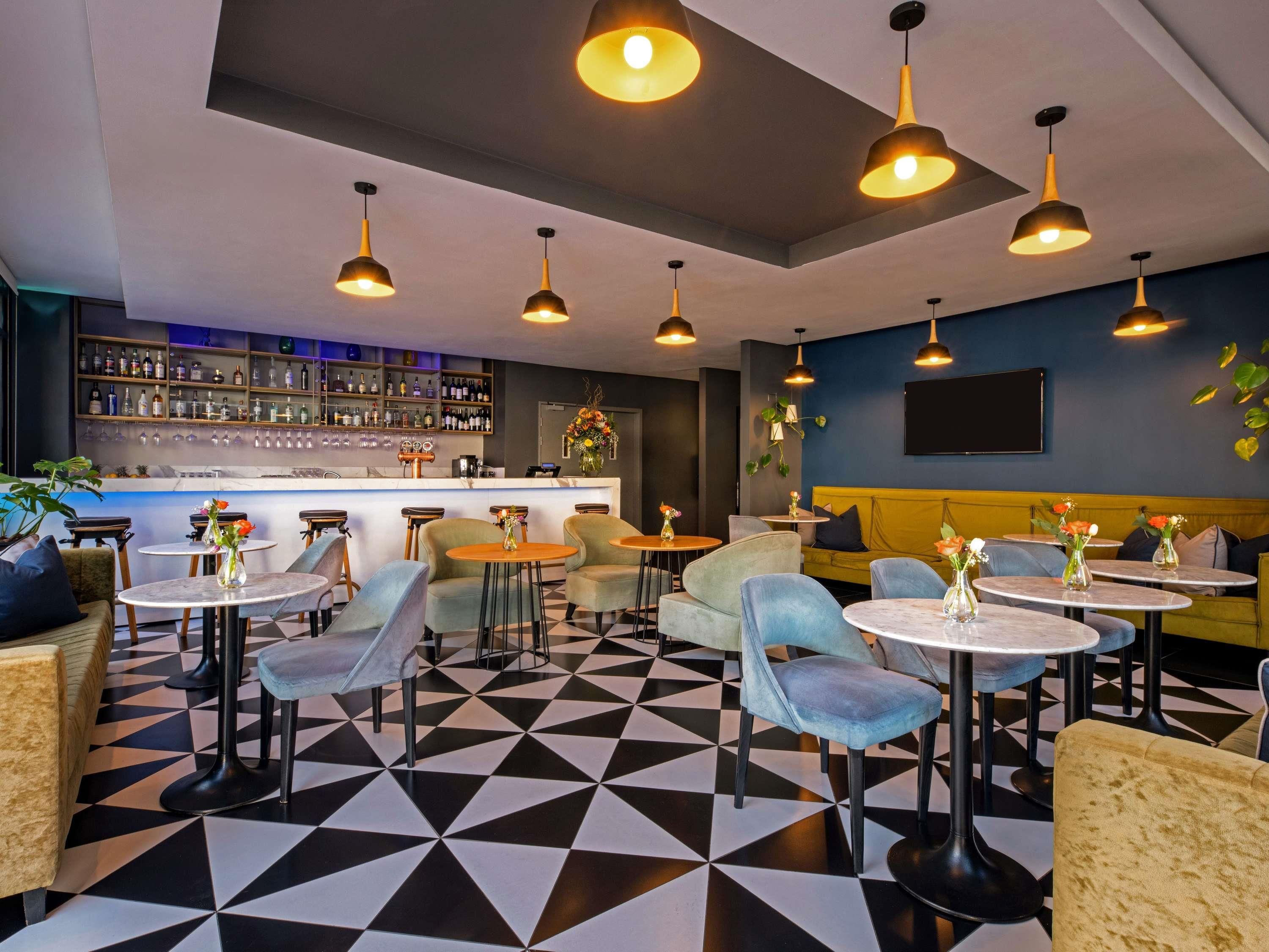 Un espace bar doté d’un sol à carreaux, de tables rondes et de luminaires suspendus.