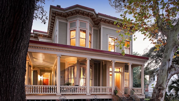 A two-story house with a porch, columns, and a red roof.