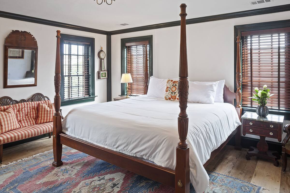 A four-poster bed with a wooden frame, a matching nightstand, a bench with cushions, and a patterned rug.