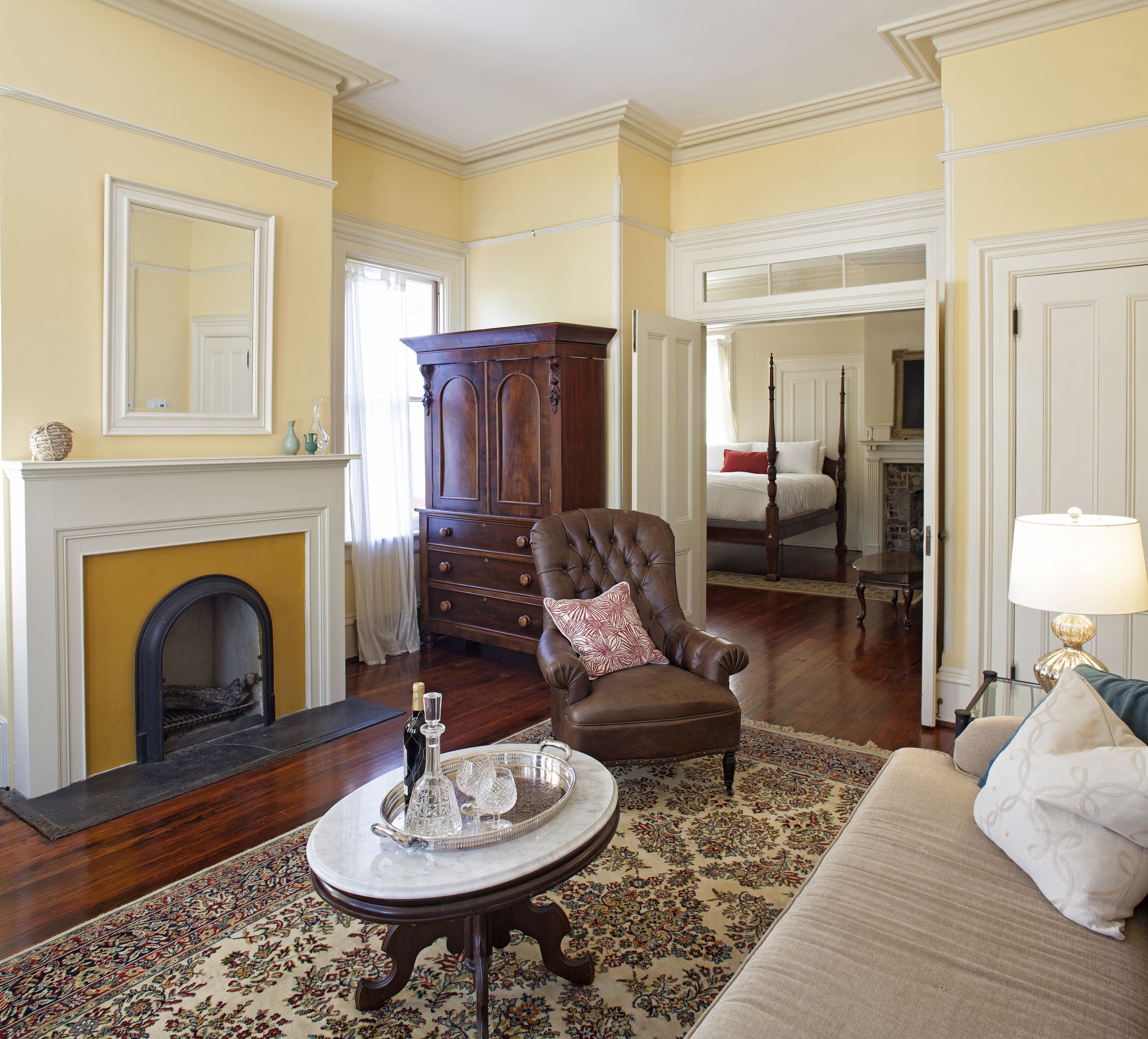 A traditional living room with a fireplace, a large wooden cabinet, a leather armchair, and a dining area with a chandelier.