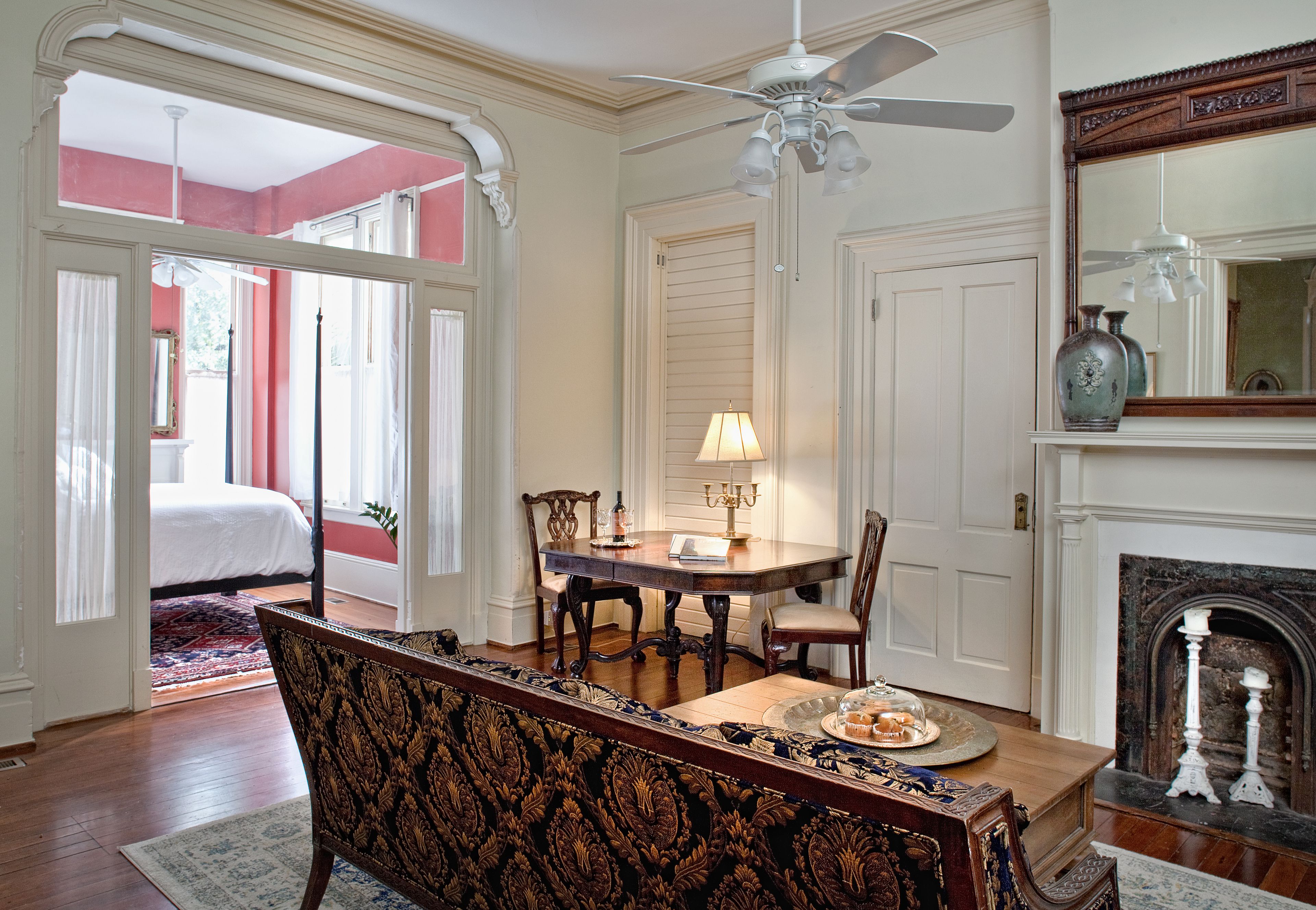 A room with a dining table, chairs, a bench, a fireplace, and a bed in the background.
