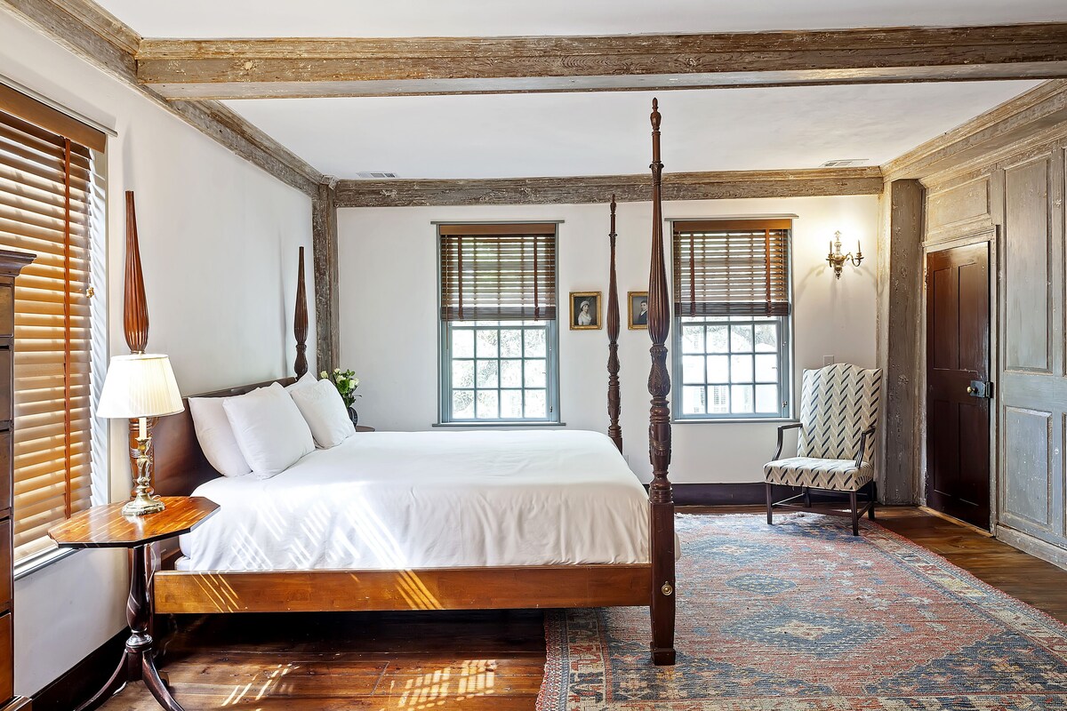 A four-poster bed with a wooden headboard, a nightstand with a lamp, and a patterned rug on a wooden floor.