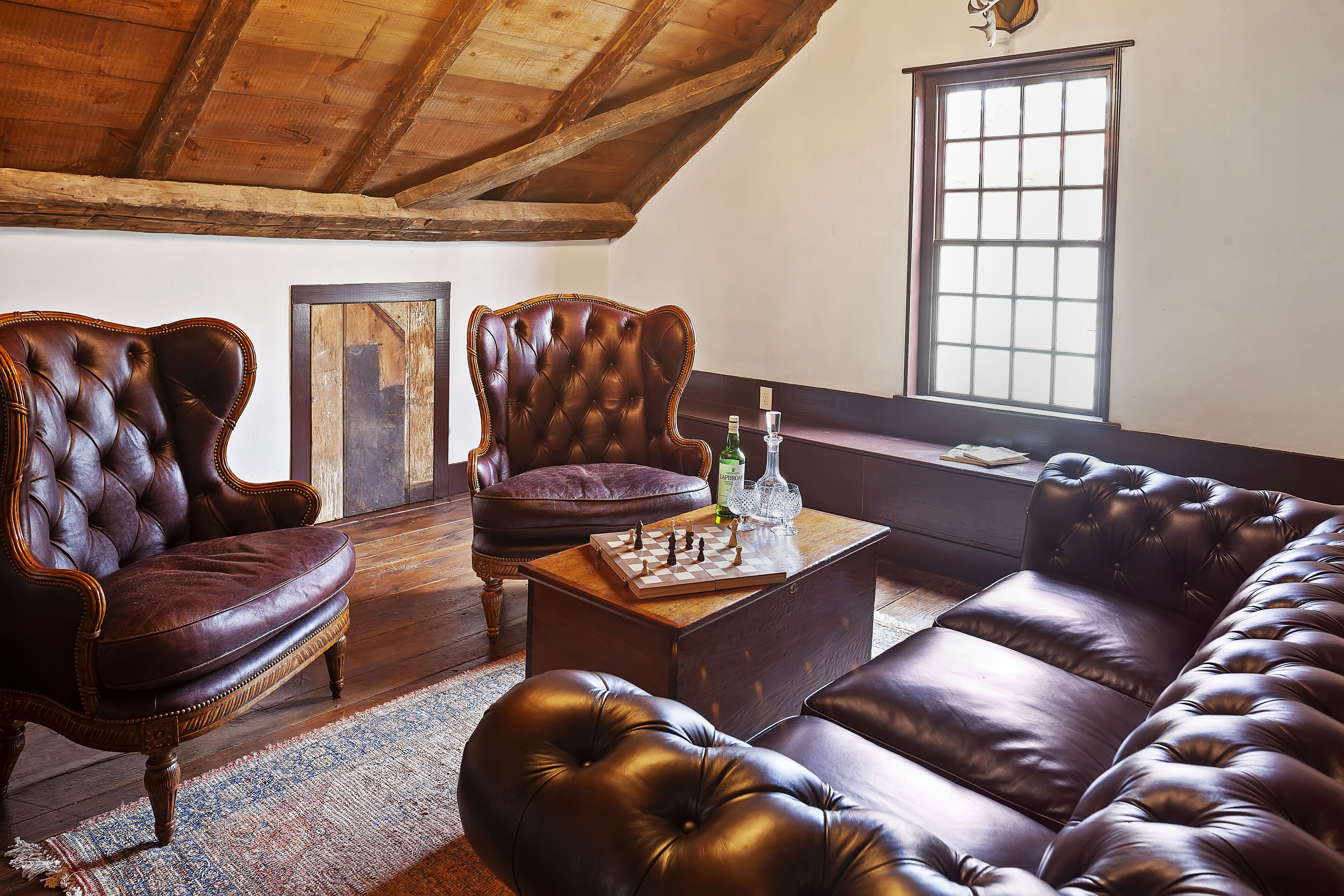 A cozy room with a wooden ceiling, leather sofas, a chessboard, and a window with a view.
