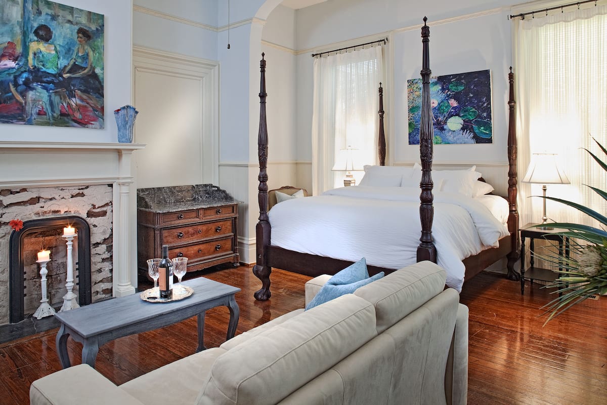 A bedroom with a four-poster bed, a fireplace, and artwork on the walls.