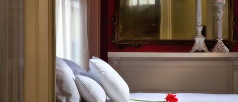 A bedroom with a bed, white pillows, a single red flower, and a mirror above the bed.