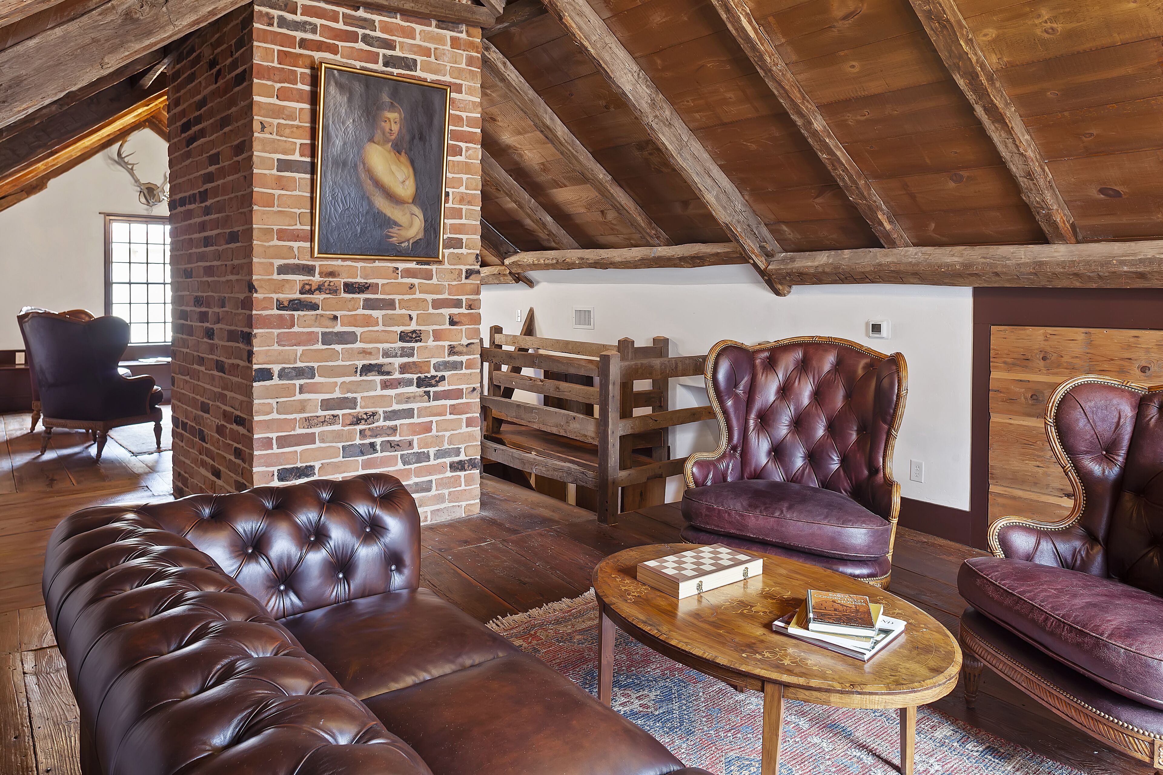 A spacious living room with a brick fireplace, leather sofas, and a wooden ceiling.