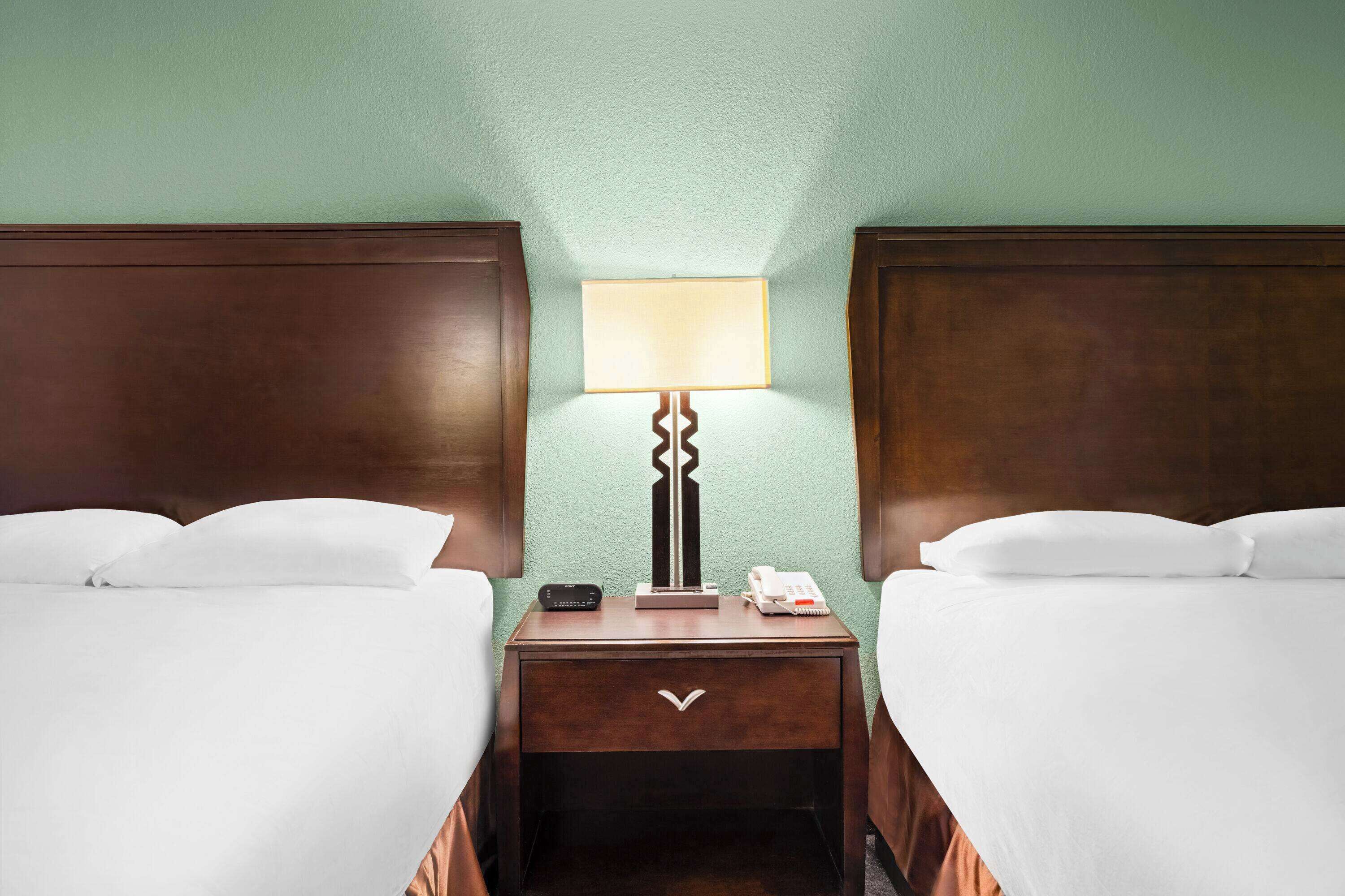 A hotel room with two single beds, a nightstand with a lamp, a telephone, and a small table.