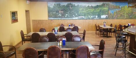 A restaurant with wooden tables and chairs, a mural of a landscape, and a clock on the wall.