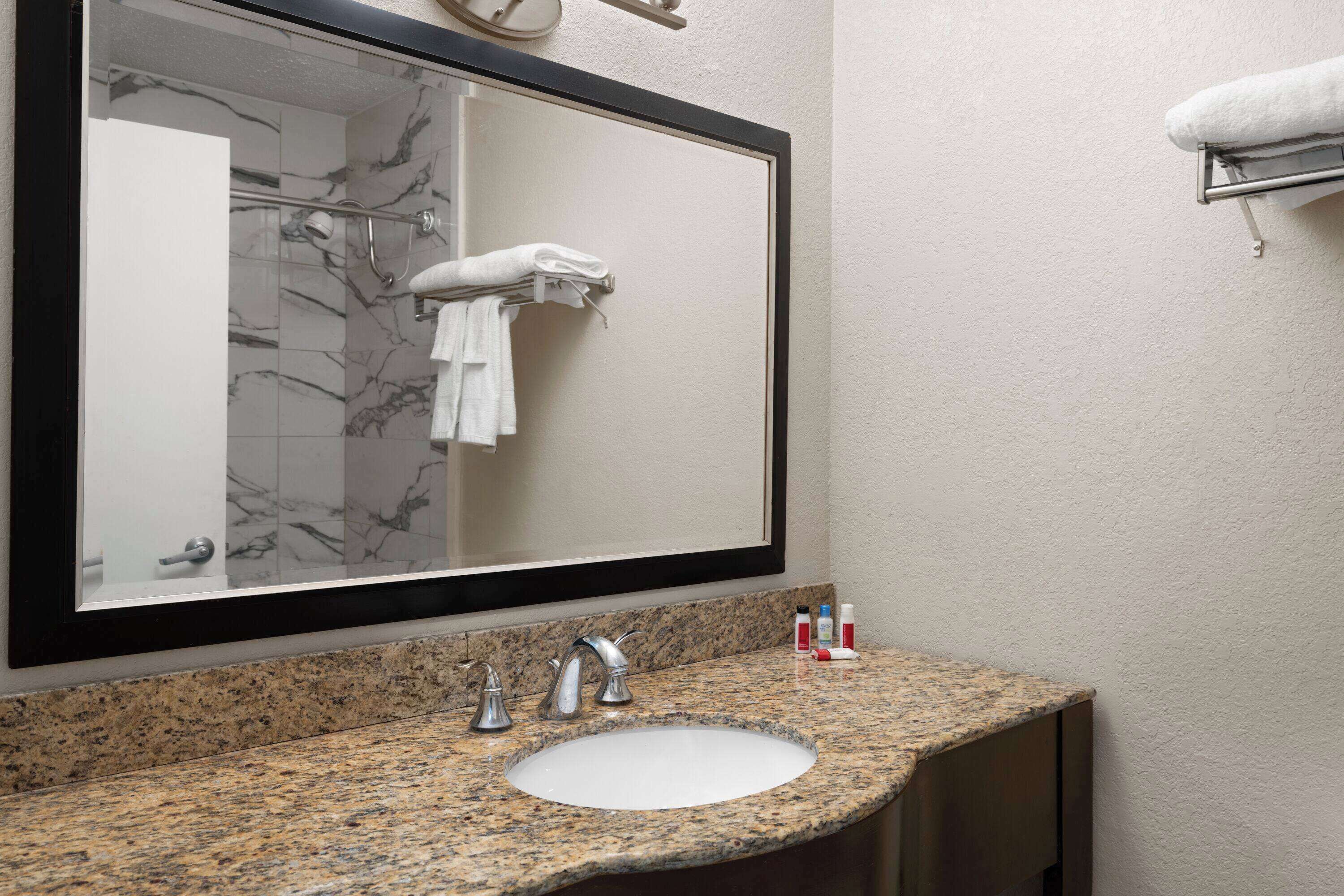 A bathroom with a granite countertop, a white sink, and a large mirror.