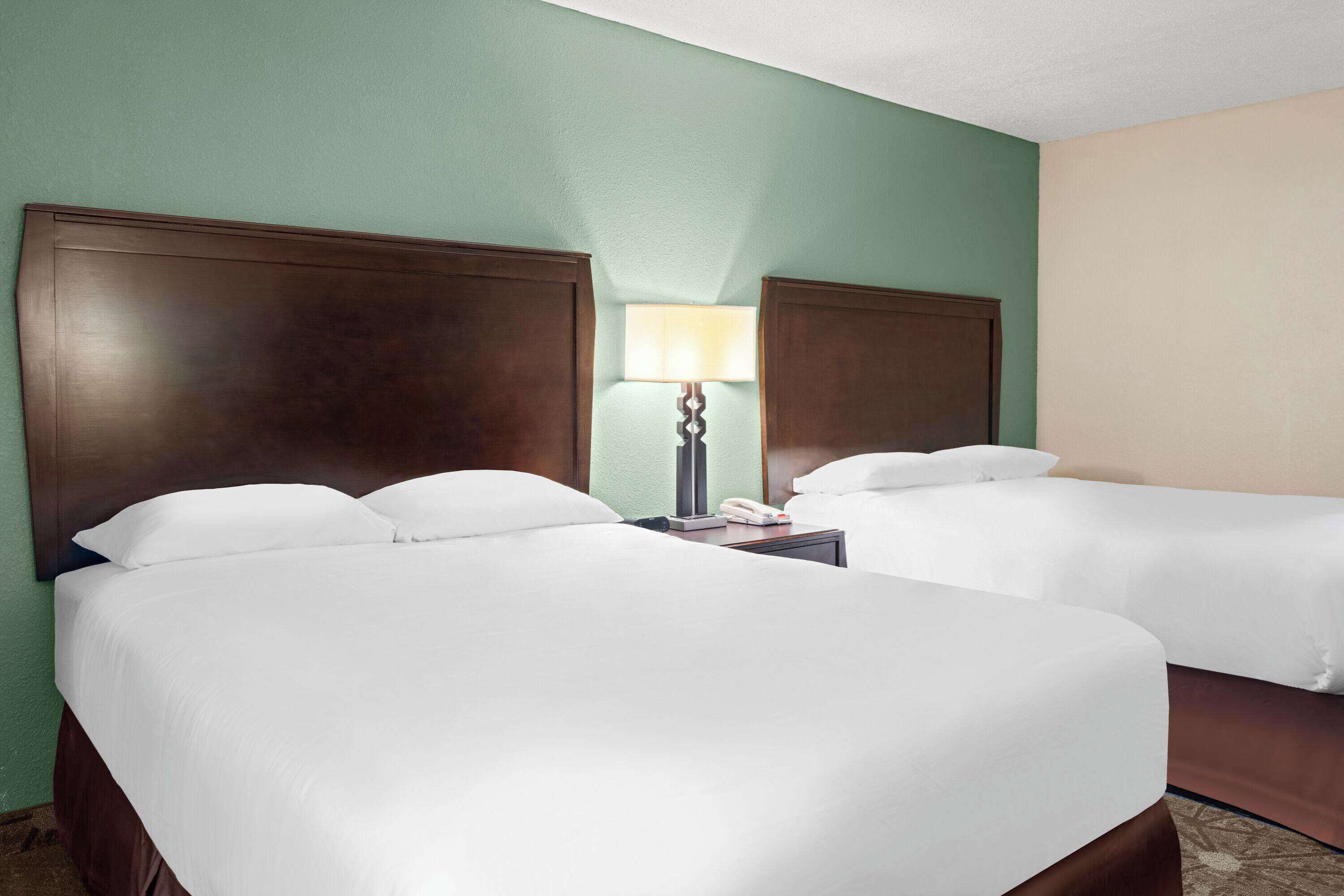 A hotel room with two beds, a nightstand with a lamp, and a telephone.