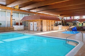 An indoor swimming pool with a wooden ceiling, a covered seating area, and a brick wall with a door. - Travelodge by Wyndham Gaylord (Gaylord)
