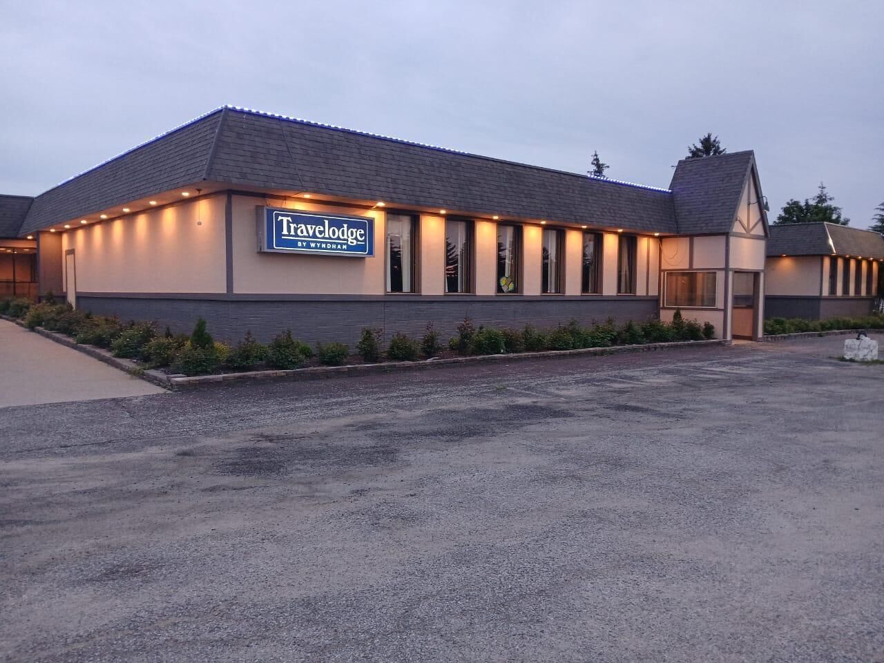 A Travelodge by Wyndham hotel with a modern design, featuring a large parking lot and a well-lit facade.